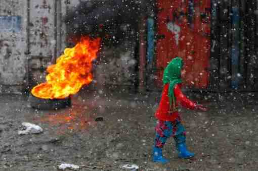 An Afghan woman walks past a burning tyre along a street on a snowy day in Kabul